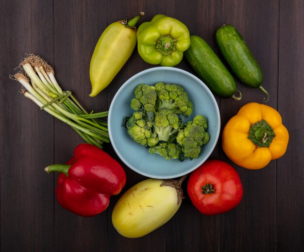 Vue de dessus le brocoli dans un bol avec des poivrons, des concombres, de la ciboulette et de la tomate sur fond de bois