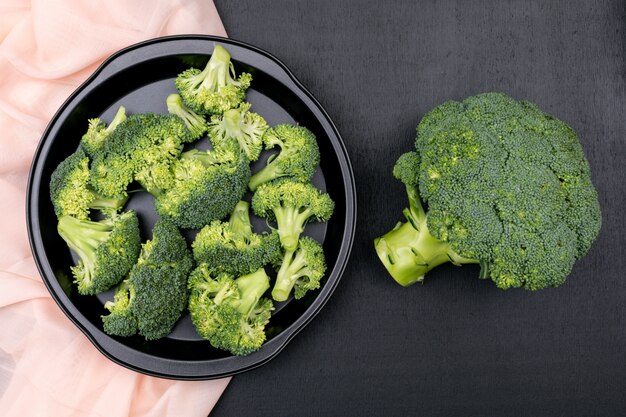 Vue de dessus de brocoli dans une casserole noire sur un tissu rose sur une surface en pierre noire