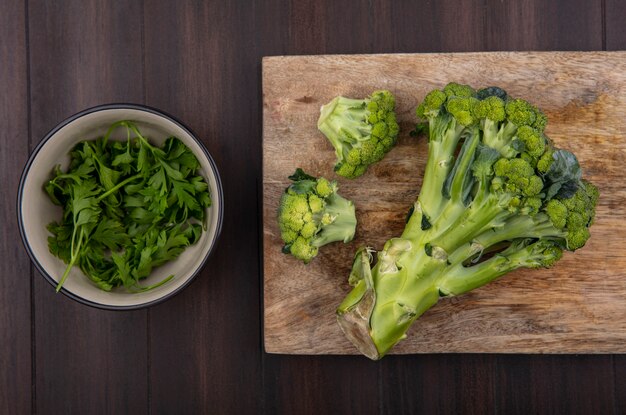 Vue de dessus le brocoli sur une planche à découper avec du persil dans un bol sur fond de bois