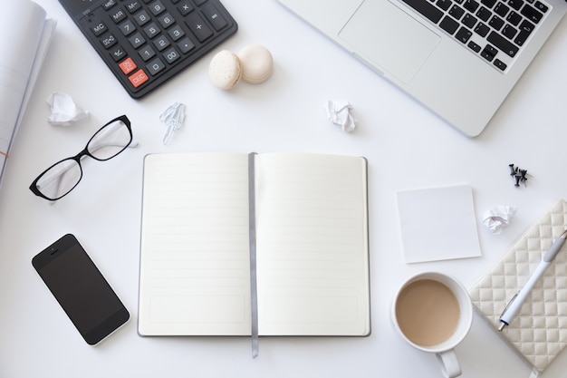 Vue de dessus d&#39;un bureau de travail avec un cahier blanc ouvert