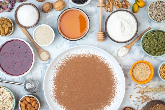 Vue de dessus cacao en poudre sur assiette ronde bols avec confiture miel farine graines de courge graines de tournesol graines de sésame amandes sur table