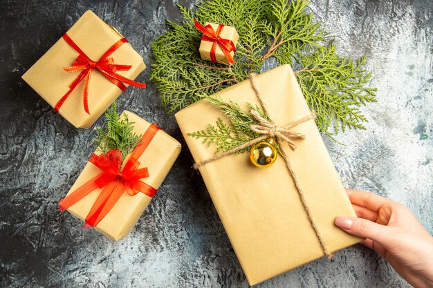 Vue de dessus cadeau de Noël en main féminine petits cadeaux branches de pin sur surface grise