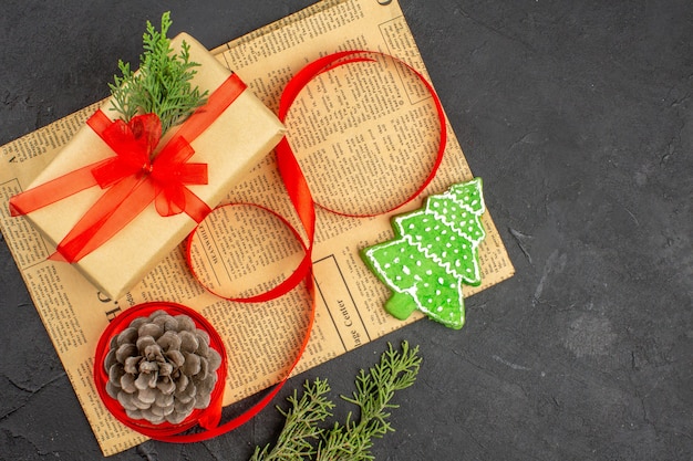 Photo gratuite vue de dessus cadeau de noël en ruban de sapin de branche de papier brun sur des ornements de noël de journal sur une surface sombre