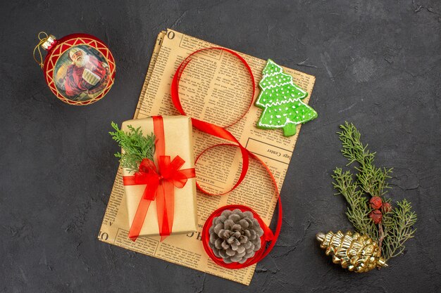 Vue De Dessus Cadeau De Noël En Ruban De Sapin De Branche De Papier Brun Sur Des Ornements De Noël De Journal Sur Une Surface Sombre