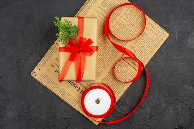 Vue de dessus cadeau de Noël en ruban de sapin de branche de papier brun sur papier journal sur une surface sombre