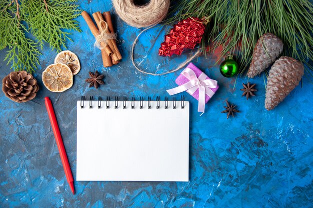 Photo gratuite vue de dessus cadeaux de noël branches de sapin cônes anis cahier crayon rouge sur surface bleue