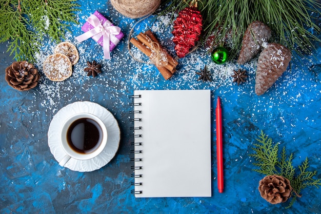 Vue de dessus cadeaux de noël branches de sapin cônes anis cahier une tasse de thé sur fond bleu place libre