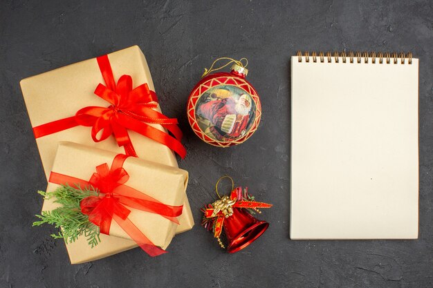 Vue de dessus des cadeaux de Noël en papier brun attaché avec un bloc-notes de jouets d'arbre de Noël en ruban rouge sur une surface sombre