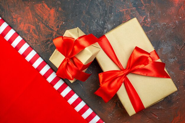Vue de dessus des cadeaux de vacances de différentes tailles attachés avec un ruban rouge sur une table rouge foncé