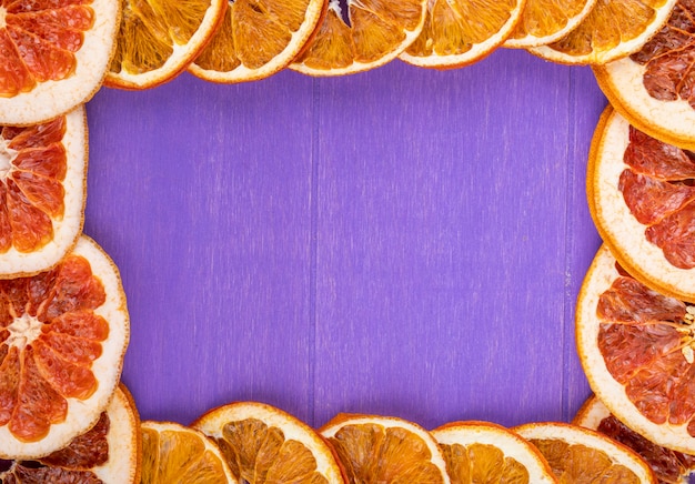 Vue de dessus d'un cadre fait de tranches d'orange et de pamplemousse séchées disposées sur un fond en bois violet avec copie espace