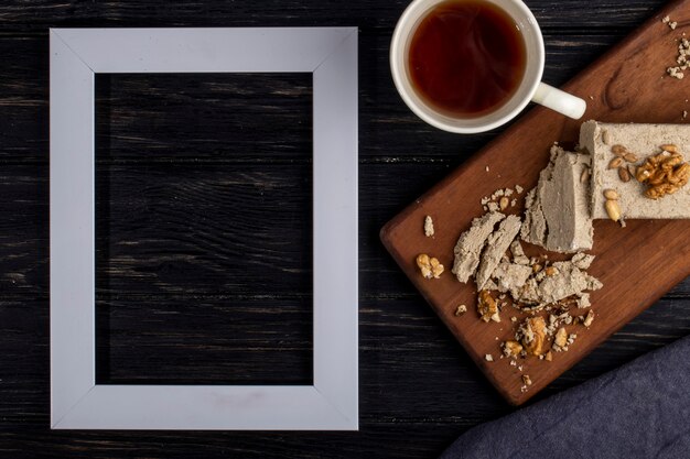 Vue de dessus d'un cadre photo vide et halva avec des graines de tournesol et des noix sur une planche de bois et une tasse de thé sur rustique