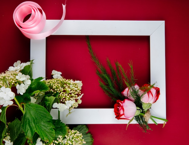 Vue de dessus d'un cadre photo vide avec des roses rouges au fenouil et viburnum en fleurs sur fond rouge