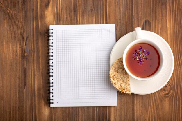 Vue de dessus cahier bleu ouvert avec une tasse de thé sur le bureau marron