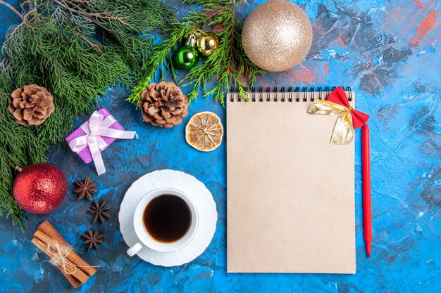 Vue de dessus un cahier branches de pin crayon rouge tasse de thé bâtons de cannelle sur fond bleu