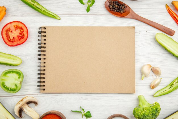 Vue de dessus cahier coupe légumes poivre noir cuillère en bois sur fond blanc