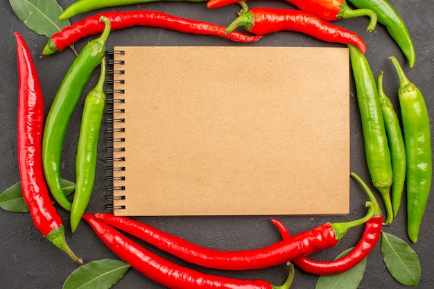 Vue De Dessus Un Cahier Dans Le Cercle Des Piments Rouges Et Verts Et Payer Les Feuilles Sur Fond Noir