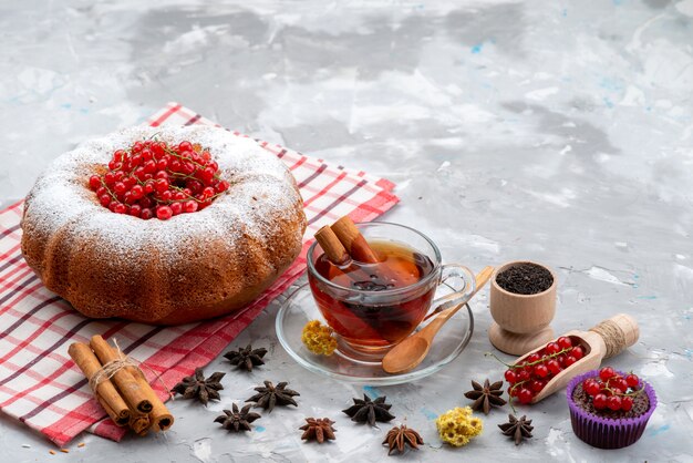 Une vue de dessus de canneberges rouges fraîches aigre-doux et moelleux avec du thé gâteau rond et de la cannelle sur le bureau blanc de fruits