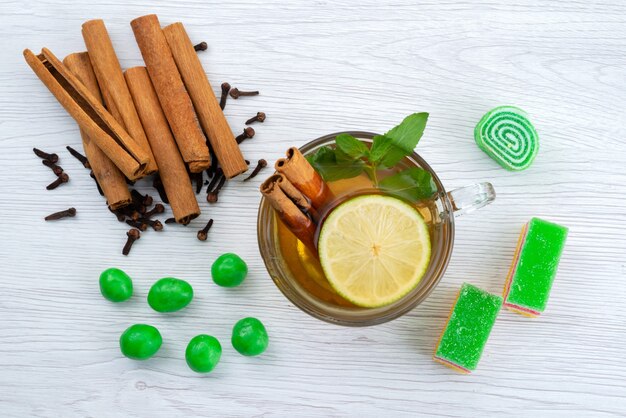 Une vue de dessus de la cannelle et du thé avec du citron et de la marmelade sur un bureau blanc, bonbons au dessert