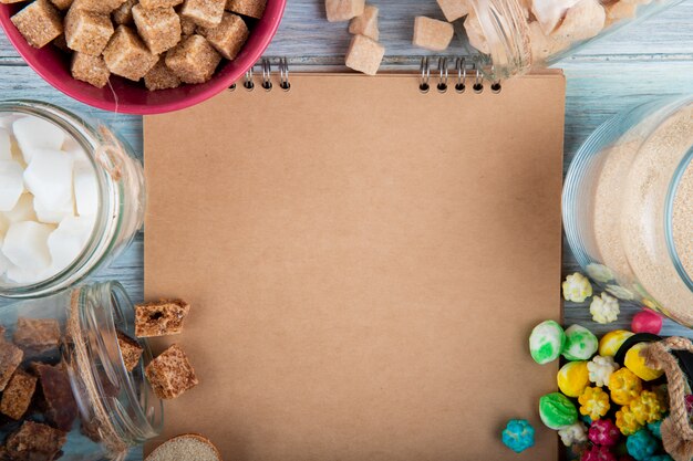 Vue de dessus d'un carnet de croquis avec différents types de sucre et de bonbons dans des bols et des bocaux en verre disposés autour sur fond rustique