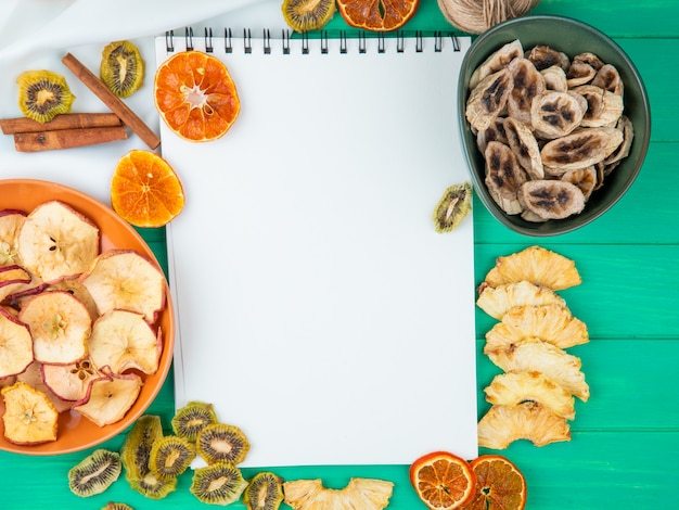 Vue de dessus d'un carnet de croquis avec diverses tranches de fruits secs et d'agrumes sur fond vert