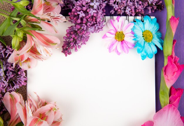 Vue de dessus d'un carnet de croquis et de fleurs de couleur rose et violet gerbera lilas alstroemeria et fleurs de marguerite sur un sac sur fond de bois violet