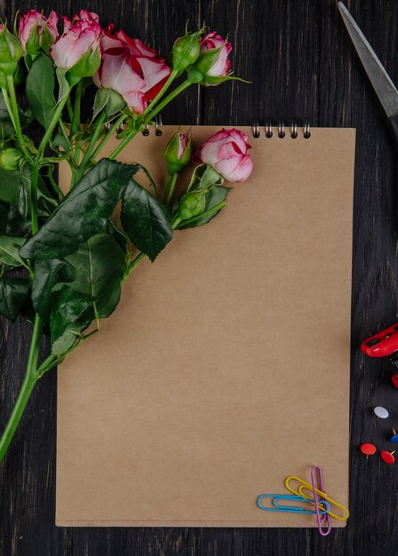 Vue de dessus d'un carnet de croquis avec des roses de couleur rose avec des bourgeons se trouvant sur un fond en bois foncé