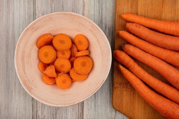 Vue de dessus de carottes très nutritives sur une planche de cuisine en bois avec des carottes hachées sur un bol sur un mur en bois gris