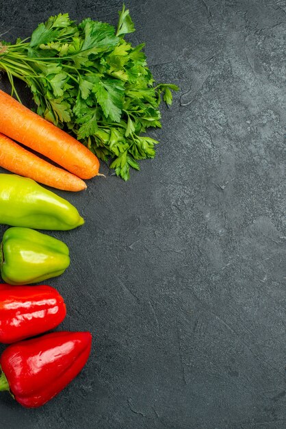 Vue de dessus des carottes vertes et des poivrons sur le côté gauche sur le tableau gris foncé