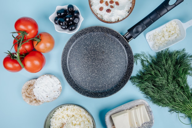 Vue de dessus d'une casserole vide et de fromage cottage dans un bol et des gâteaux de riz avec du fromage à la crème avec de l'aneth tomates fraîches et des olives marinées sur bleu