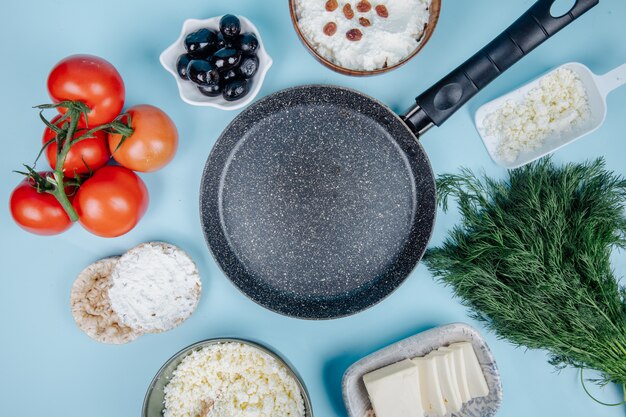 Vue de dessus d'une casserole vide et de fromage cottage dans un bol et des gâteaux de riz avec du fromage à la crème avec de l'aneth tomates fraîches et des olives marinées sur bleu