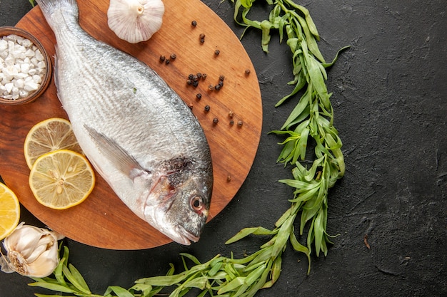 Vue de dessus cercle d'estragon autour de poisson cru frais sel de mer à l'ail dans un bol sur une planche de bois ronde sur fond noir