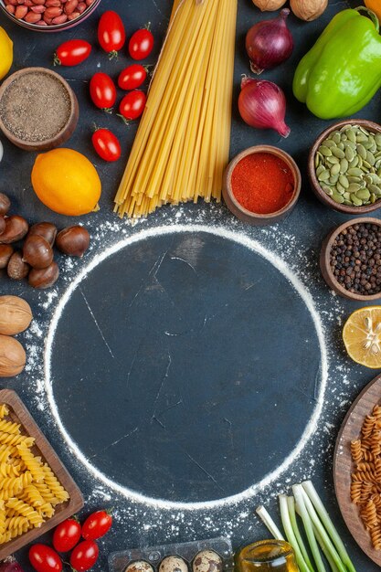 Vue de dessus cercle de farine autour des oeufs légumes pâtes noix et assaisonnements sur fond sombre photo couleur repas régime alimentaire cru