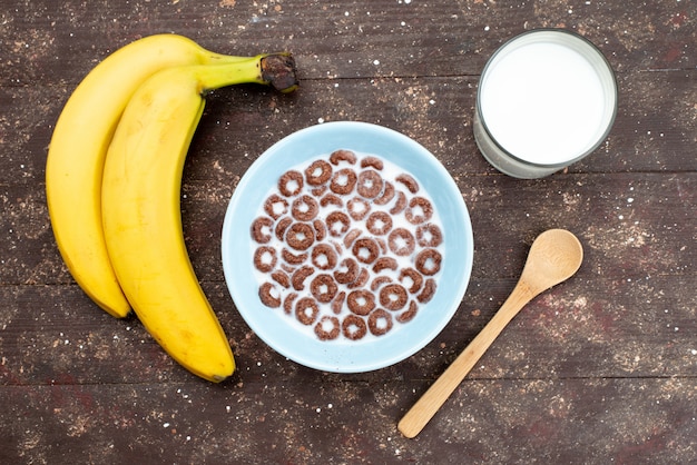 Vue de dessus des céréales au chocolat avec du lait à l'intérieur de la plaque bleue et avec des bananes sur brown