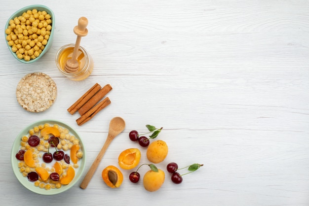 Vue de dessus des céréales avec du lait à l'intérieur de la plaque avec des craquelins fruits à la cannelle et du miel sur blanc, boire le petit déjeuner de crémerie lait