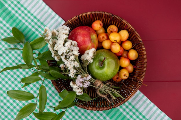 Vue de dessus cerise blanche avec des pommes et des fleurs colorées dans un panier sur une table rouge