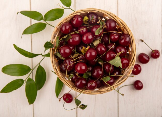 Vue de dessus des cerises dans le panier avec des feuilles sur fond de bois