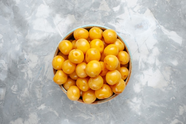 Photo gratuite vue de dessus cerises jaunes à l'intérieur de la plaque brune sur la photo couleur de fruits de bureau gris clair