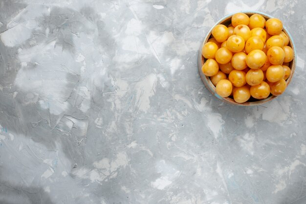 Vue de dessus les cerises jaunes à l'intérieur de la plaque ronde sur le fond gris fruits frais couleur photo douce