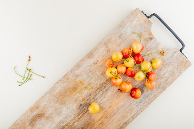 Vue de dessus des cerises sur une planche à découper avec des tiges sur une surface blanche