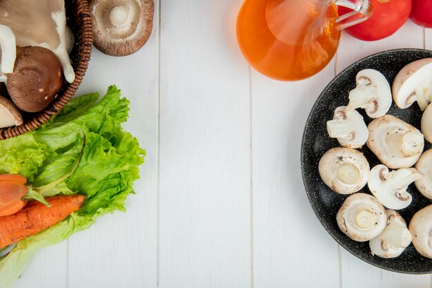 Vue de dessus des champignons blancs frais sur une assiette et des carottes fraîches bouteille d'huile d'olive sur blanc avec copie espace