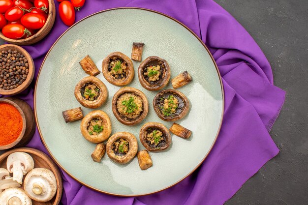 Vue de dessus des champignons cuits à l'intérieur de la plaque avec des assaisonnements sur le plat de tissu violet repas cuisson dîner aux champignons