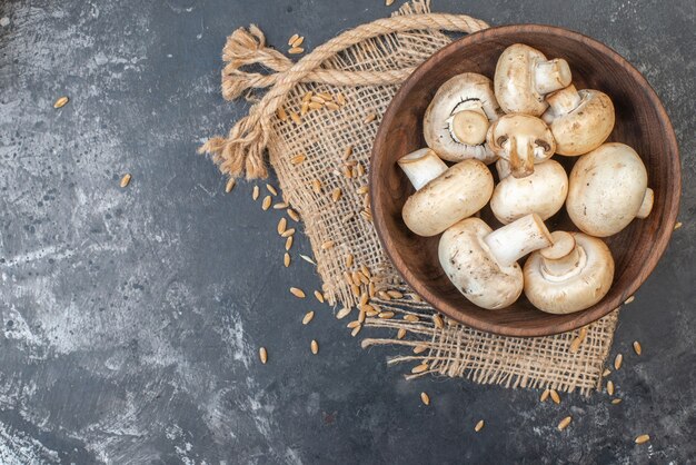 Vue de dessus des champignons dans un bol d'ail dispersés sur une corde de grains de blé sur un lieu de copie de table grise