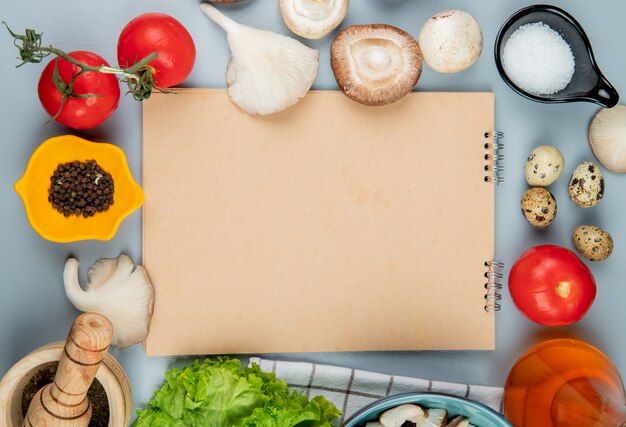 Vue de dessus des champignons frais aux tomates poivre noir, oeufs de caille et sel disposés autour d'un carnet de croquis sur bleu clair