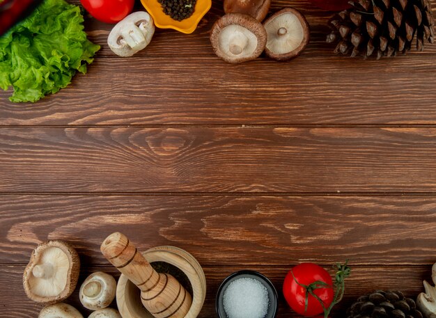 Vue de dessus de champignons frais avec des grains de poivre noir tomates fraîches mortier en bois avec des herbes séchées sel et cônes sur bois rustique avec espace copie