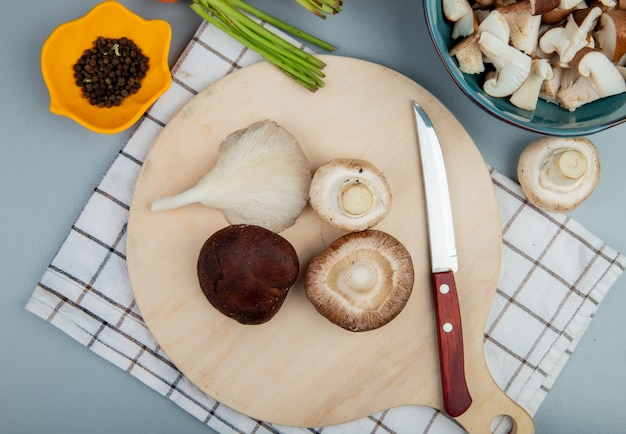 Photo gratuite vue de dessus des champignons frais sur une planche à découper en bois avec un couteau de cuisine sur bleu clair avec des carottes fraîches sur bleu clair