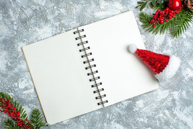 Vue de dessus chapeau de Noël aux baies rouges de Noël sur le bloc-notes sur un tableau blanc gris