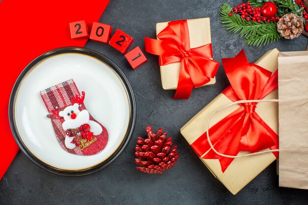 Vue de dessus de chaussette de Noël sur une assiette de branches de sapin conifère cône numéros beaux cadeaux sur une table sombre