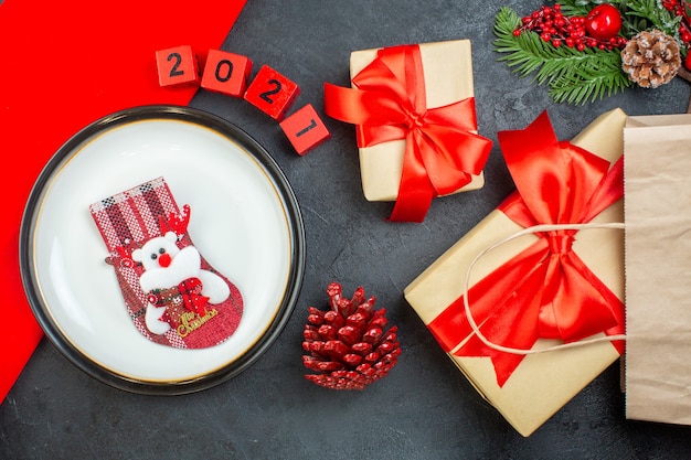 Vue de dessus de chaussette de Noël sur une assiette de branches de sapin conifère cône numéros beaux cadeaux sur une table sombre