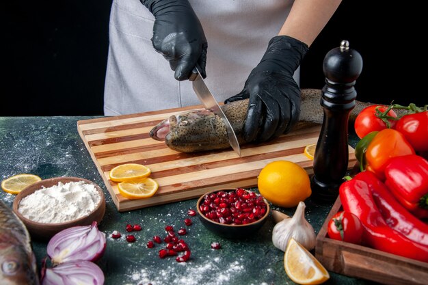 Vue de dessus chef coupant la tête de poisson sur une planche à découper moulin à poivre bol de farine graines de grenade dans un bol de légumes sur la table de la cuisine