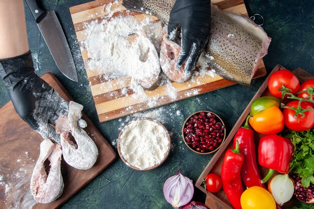 Vue de dessus chef couvrant des tranches de poisson cru avec de la farine de légumes frais sur un bol de farine de planche de bois sur la table de la cuisine